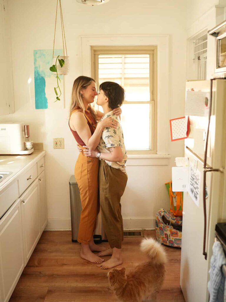 Cassie and Sienna dancing together in their kitchen during a cozy queer at-home couples photography session.